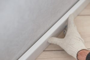 biała rękawiczka na ręce osoby, która montuje listwy przypodłogowe kasolik